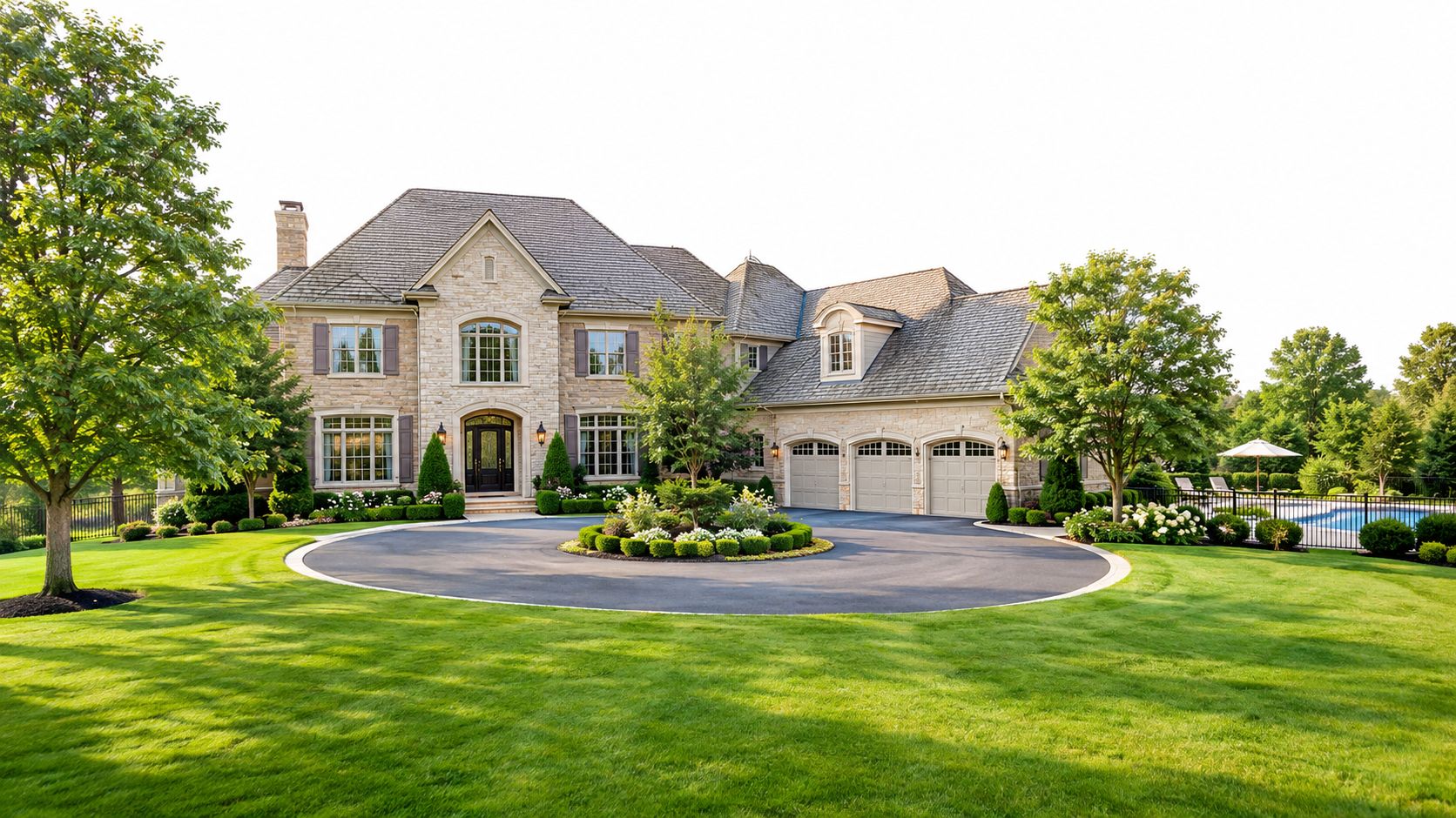 A luxurious stone mansion with a circular driveway and manicured lawn in a lush landscape.