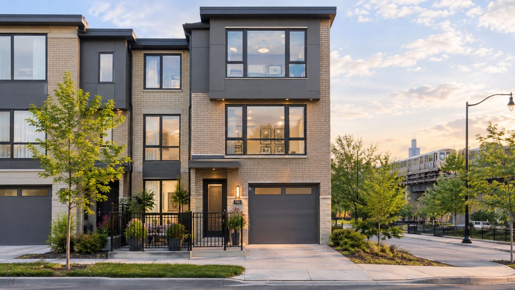A modern three-story townhome with a garage, private patio, and a train passing in the background.