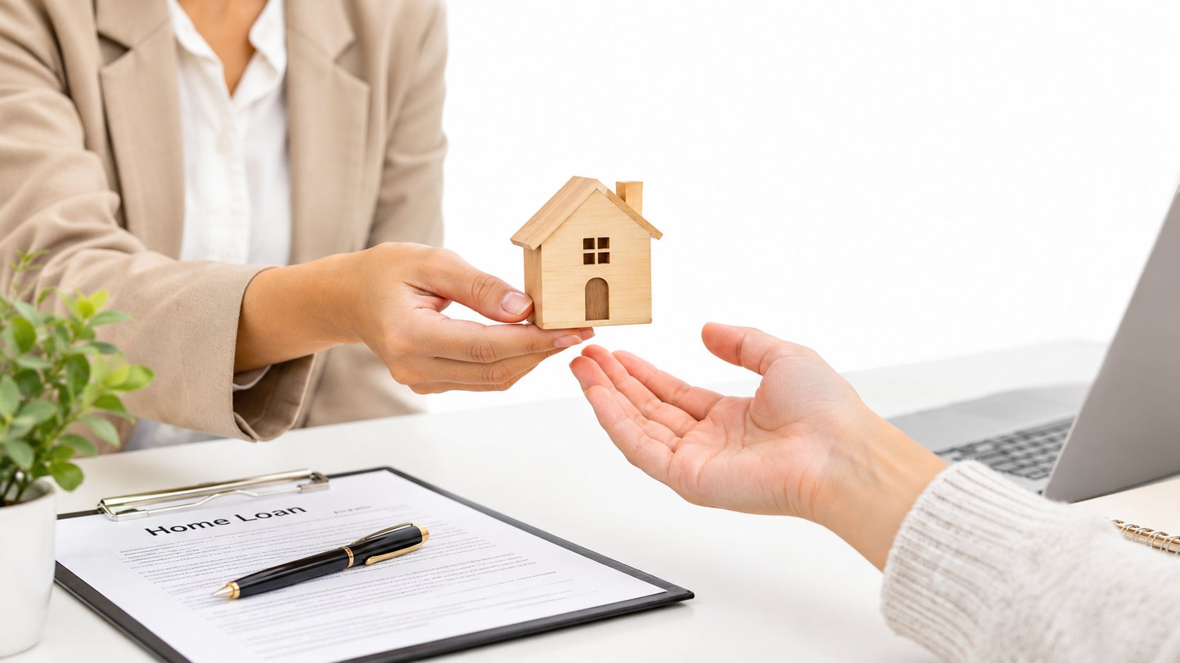 A loan officer handing a small wooden house model to a first time home buyer client.